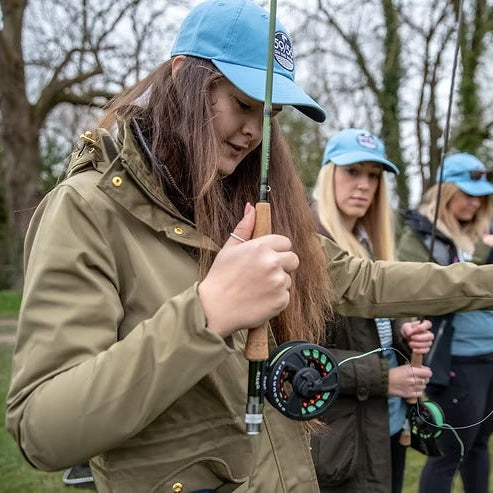 People fishing outdoors with a focus on a woman holding a fishing rod.
